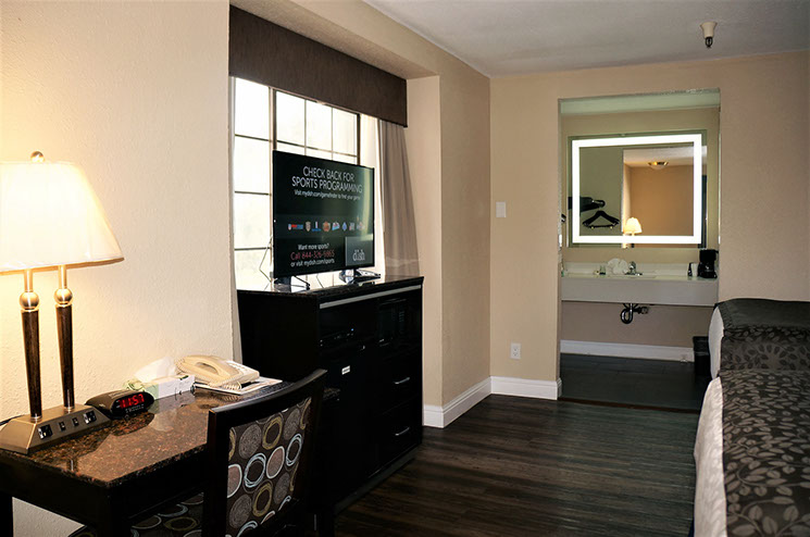 Photo showing 2 double beds, writing table and chair with lamp, alarm clock and telephone. A wooden chest of drawers and flat screen television.